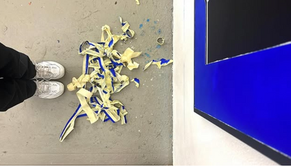 Ansicht von oben auf einen betonierten Fussboden. Dort liegen die abgerissenen Klebestreifen von der berarbeitung des Gemäldes 